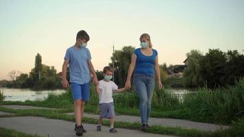 A family with a child in medical masks walk near the lake