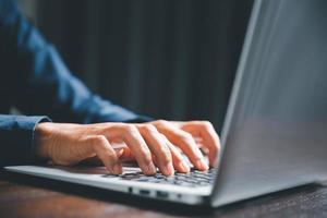 Closeup of businesswoman typing on laptop computer while sitting on table in office for design work, insert icons or business technology symbols. selective focus on hand. female online working on desk photo