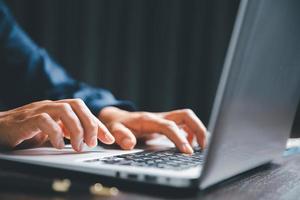 Closeup of businesswoman typing on laptop computer while sitting on table in office for design work, insert icons or business technology symbols. selective focus on hand. female online working on desk photo