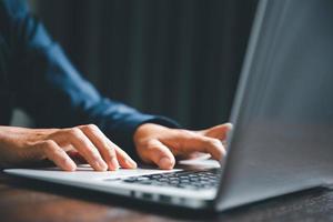 Closeup of businesswoman typing on laptop computer while sitting on table in office for design work, insert icons or business technology symbols. selective focus on hand. female online working on desk photo