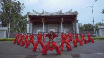 A Chinese teenager in a red costume dancing using a stick in front of the temple video