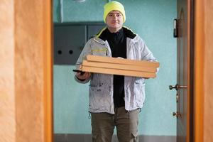 Delivery man with pizza cardboard boxes. Courier in green color hat standing against door of residential house photo