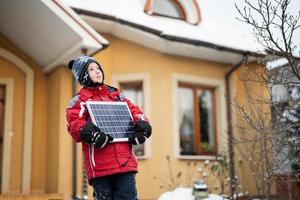 chico con panel solar contra casa en invierno. concepto de energía alternativa. foto
