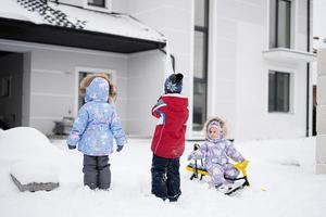 los niños juegan al aire libre en la nieve. tres niños disfrutan de un paseo en trineo. trineo infantil en invierno contra la casa. foto