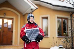 chico con panel solar contra casa en invierno. concepto de energía alternativa. foto