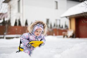 Baby girl play outdoors in snow, enjoy a sleigh ride. Child sledding. Toddler kid riding a sledge. Sled in winter. photo