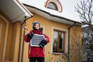 chico con panel solar contra casa en invierno. concepto de energía alternativa. foto