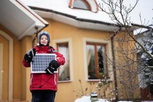 chico con panel solar contra casa en invierno. concepto de energía alternativa. foto