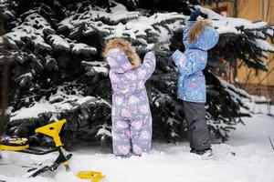 Children play outdoors in snow. Two little sisters near Christmas tree in winter. photo