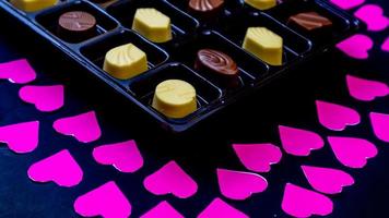 delicioso chocolate rodeado de corazones rosas sobre fondo negro foto