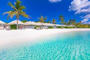villas de playa en maldivas, viajes de verano de lujo y fondo de vacaciones. increíble mar azul y palmeras bajo el cielo azul. paisaje tropical y playa exótica. destino de vacaciones de verano o luna de miel foto