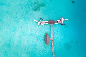 Beautiful aerial view of Maldives jetty seaplane top view with wooden boat and tropical beach. Luxury tropical resort or hotel with water villas and beautiful beach scenery. Amazing bird eyes view photo