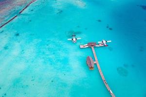Beautiful aerial view of Maldives jetty seaplane top view with wooden boat and tropical beach. Luxury tropical resort or hotel with water villas and beautiful beach scenery. Amazing bird eyes view photo