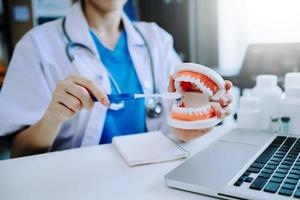 Dentist sitting at table with jaw samples tooth model and working with tablet and laptop in dental office professional dental clinic. photo