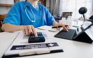 Healthcare costs and fees concept.Hand of smart doctor used a calculator and smartphone, tablet for medical costs at hospital in morning light photo