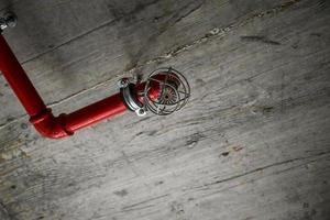 A detail of a rustic ceiling with red pipes and a fire alarm photo