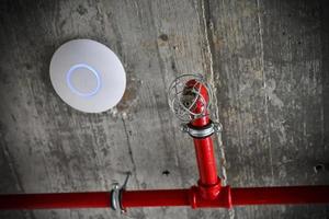 A detail of a rustic ceiling with red pipes and a fire alarm photo