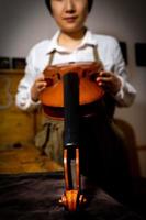 young chinese woman violin maker checking the quality of her violin in the workshop photo