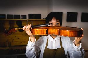 young chinese woman violin maker checking the quality of her violin in the workshop photo