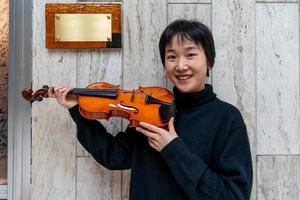 young Chinese female violin maker showing her freshly made violin outdoors photo