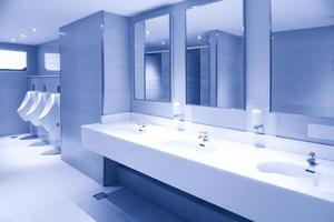 Descarga de urinarios de la habitación de los hombres, inodoro en un baño moderno, lavabo del inodoro interior del baño público con lavado de manos y espejo foto