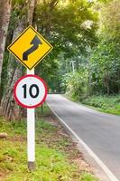 señal de tráfico de límite de velocidad selectiva 10 y símbolo de precaución de carretera sinuosa para la conducción segura en carretera rural en bosque con vistas a la montaña, clave baja foto