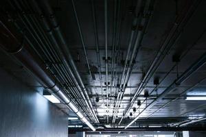 Tuberías de sistema sanitario y cables eléctricos instalados bajo estructura de hormigón armado de losa plana en edificio. Tuberías de ventilación en estacionamiento subterráneo foto