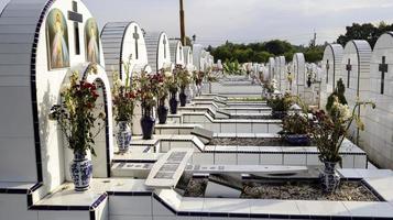 el cementerio público contiene tumbas idénticas de cerámica blanca con flores. foto