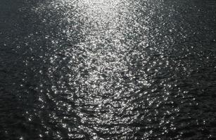 superficie del agua con olas y ondas y la luz del sol reflejada en la superficie. foto