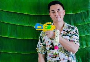 Thai man holding water gun and jasmine garland to give blessing for Songkran festival with banana leaf background. photo