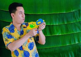 hombre tailandés sosteniendo una pistola de agua para el festival songkran con fondo de hoja de plátano. foto