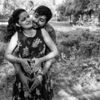 Indian couple posing for maternity baby shoot. The couple is posing in a lawn with green grass and the woman is falunting her baby bump in Lodhi Garden in New Delhi, India - Black and White photo