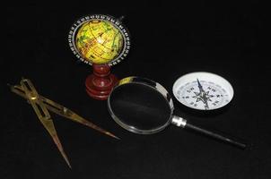 Compass, globe and magnifying glass on black background photo