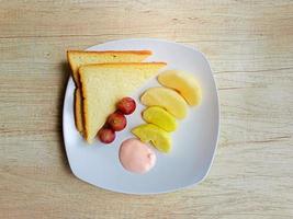 Healthy food of fresh fruits and slice of bread on white plate on table, top view photo