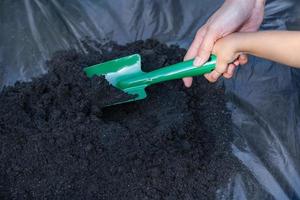 Close-up of toddler son and mother's hand teaching little son preparing soil to plant in garden, mother and son relationship. Mommy's little helper. Gardening. Leisure activities concept photo