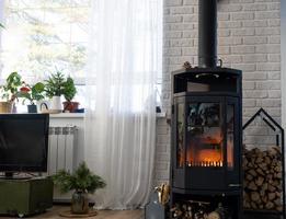 Black stove, fireplace in interior of house in loft style. Alternative eco-friendly heating, warm cozy room at home, burning wood photo