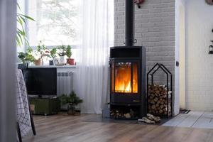 Black stove, fireplace in interior of house in loft style. Alternative eco-friendly heating, warm cozy room at home, burning wood photo