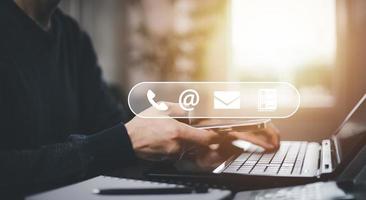 Communication and Contact us or Customer support hotline people connect. Hand using a laptop and touching on virtual screen contact icons, email and address, live chat with internet wifi. photo