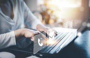 Communication and Contact us or Customer support hotline people connect. Hand using a laptop and touching on virtual screen contact icons, email and address, live chat with internet wifi and market photo