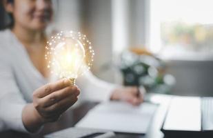 Woman hand hold light bulb with icons work on the desk, Creativity and innovation are keys success. Concept of new idea and innovation with icons and light bulbs, Save the money, Freedom of thought. photo