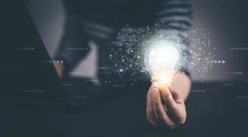 Businessman hand holding light bulb with icons and working on the desk, Creativity and innovation are keys to success.Concept of new idea and innovation with energy and power , working at home, photo