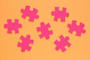 Pink mosaic game details of jigsaw puzzle elements on orange background. Completing task or solving problem concept. World mental health day, autism awareness day. Global communication. Hobby, play photo