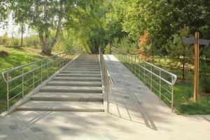 Stairs and ramp with metal railings for the passage of strollers and wheelchairs in public park. Concept of comfortable barrier-free urban environment in city. Pathway for people with disabilities photo