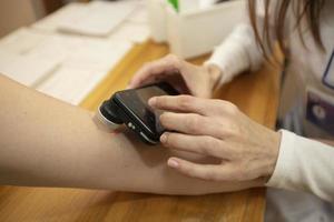 Doctor dermatologist examining birthmarks and moles on a female patient's hand. Close up cropped image of examination of birthmarks with modern device, using light and phone application and camera photo