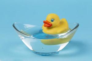 A yellow rubber duck floats in a bath on a blue background. photo