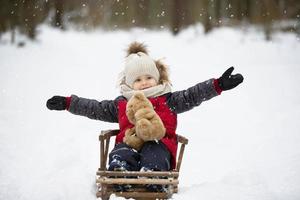 A little boy sits in a wooden sled against the backdrop of winter nature. photo