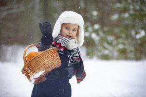 A little boy carries a basket of oranges through the winter forest. Child with fruits in winter. photo