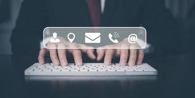 Communication and Contact us or Customer support hotline people connect. Businessman Hand using a laptop and touching on virtual screen contact icons, email and address, live chat with internet wifi. photo