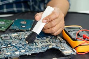 El técnico usa un cepillo y una bola de aire para limpiar el polvo en la placa de circuito de la computadora. reparación de tecnología de actualización y mantenimiento. foto