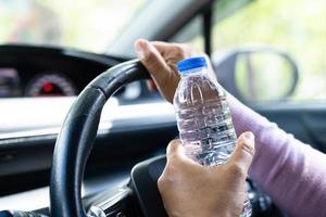 Asian woman driver holding bottle for drink water while driving a car. Plastic hot water bottle cause fire. photo